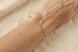 Bracelet femme doré style La Vie en Or porté au poignet sur fond lin crème