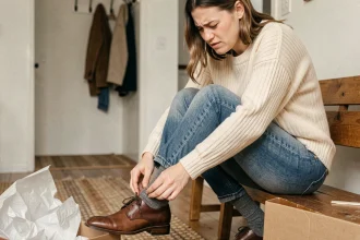 Femme enfilant une chaussure en cuir neuve trop serrée assise sur un banc en bois
