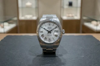 Rolex Datejust 36 posée sur une surface en ardoise noire dans une boutique de luxe minimaliste, vue de dessus avec détail précis du cadran argenté et du bracelet jubilé